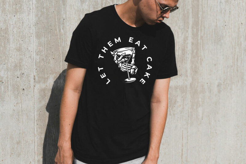 Image of model against concrete wall in black t-shirt with an illustration of a skeleton hand gripping martini glass and text in a semi-circle that reads "Let Them Eat Cake".